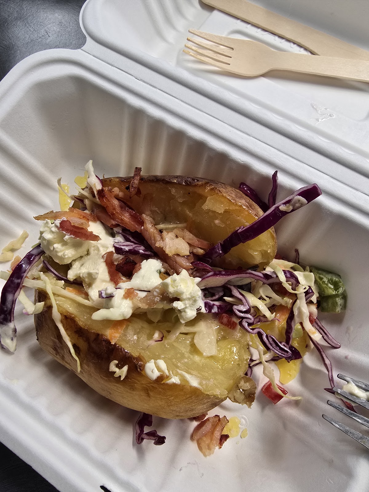 A loaded baked potato with slaw, bacon and sauce in a takeaway box